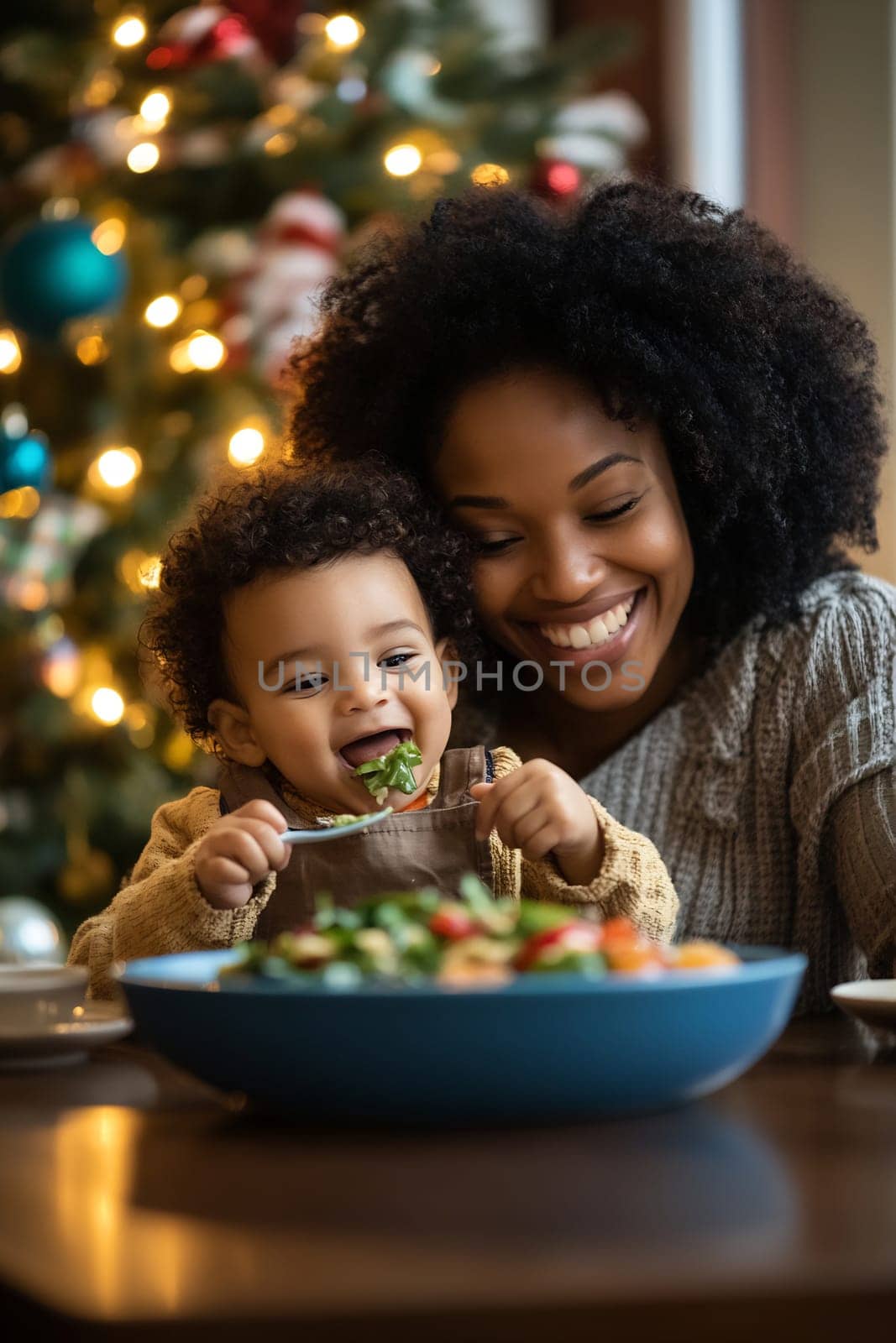 A mother smiles as her toddler enjoys a vibrant salad at a table adorned with holiday decorations, creating a warm family atmosphere.