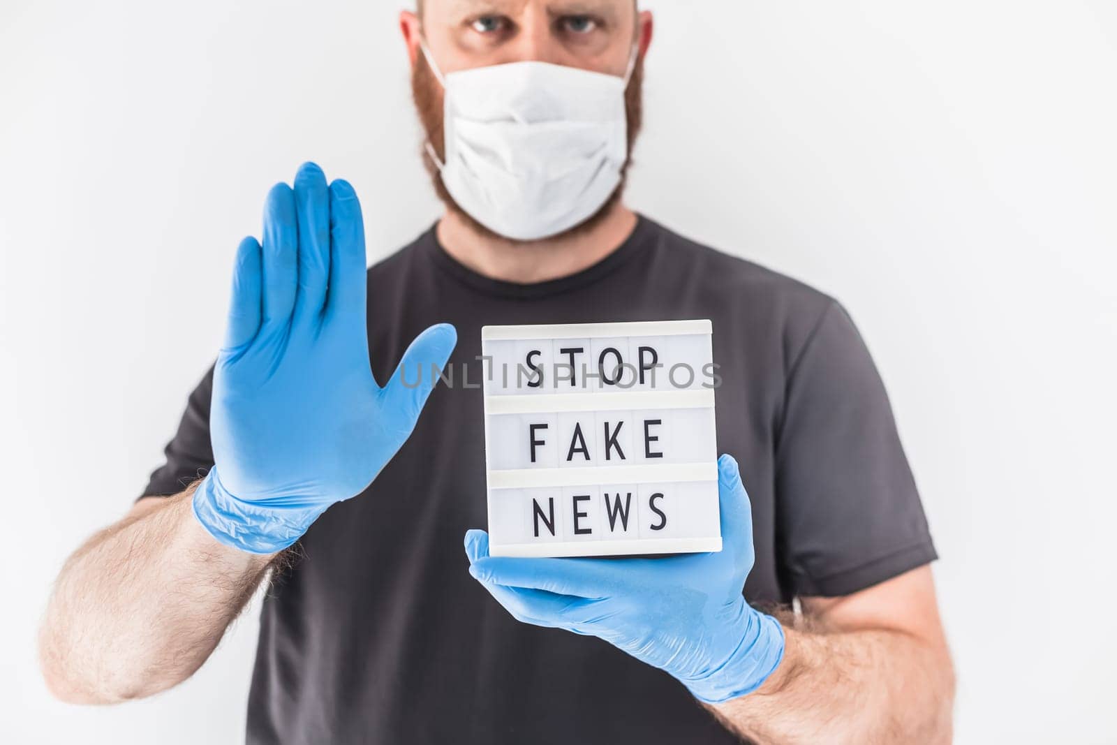 Fake news infodemics during Covid-19 pandemic concept. Man wearing protective mask and medical gloves on hands holding lightbox with text Stop fake news. People want to know truth about coronavirus
