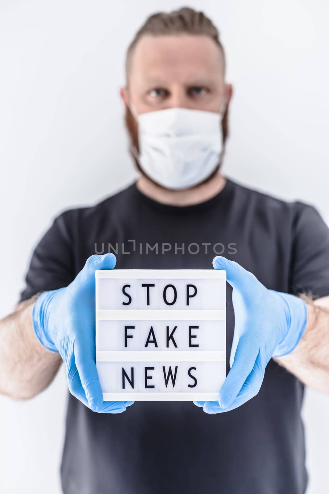 Fake news infodemics during Covid-19 pandemic concept. Man wearing protective mask and medical gloves on hands holding lightbox with text Stop fake news. People want to know truth about coronavirus