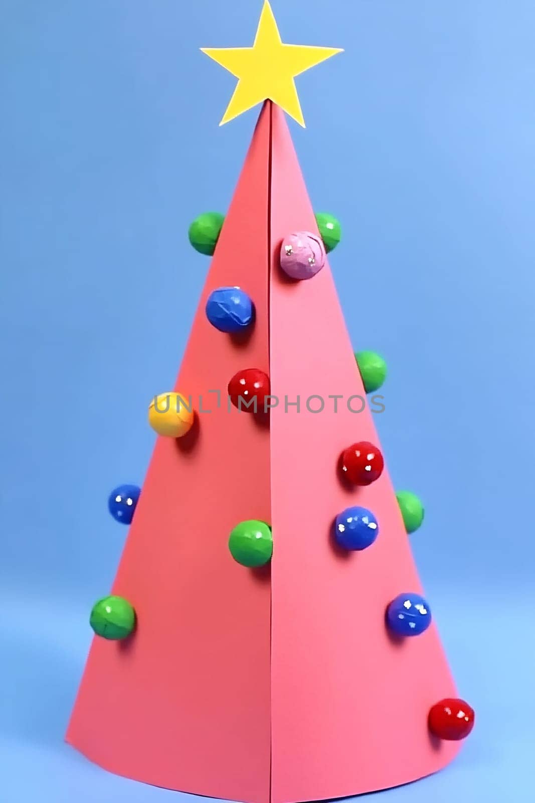 A handmade paper Christmas tree stands upright, adorned with colorful ornaments and topped with a bright star, set against a blue backdrop.