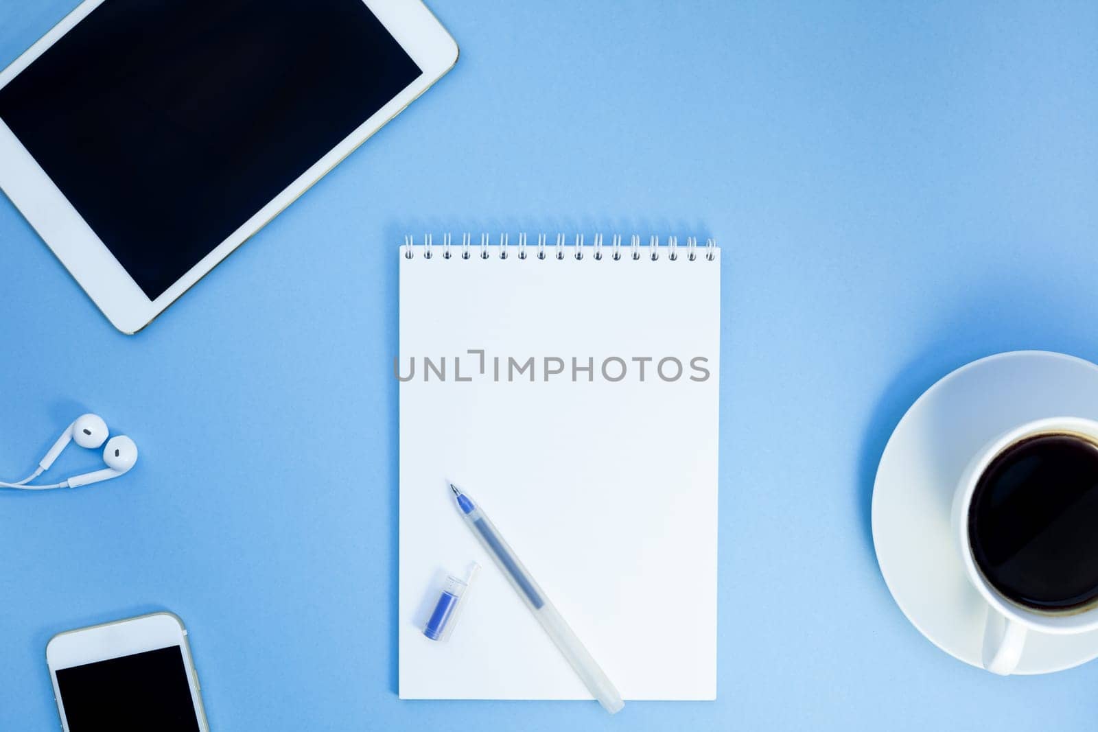 Creative flat lay photo of workspace desk with paper notebook, smartphone, earpieces, pen and coffee with copy space background minimal style