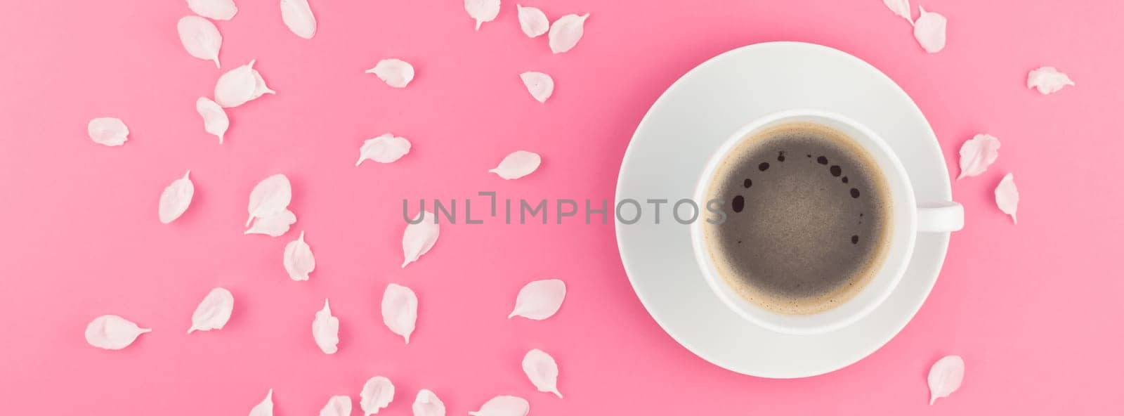 Creative flat lay concept top view of coffee cup and white apple tree flowers petals on pastel pink background with copy space in minimal style, long wide banner