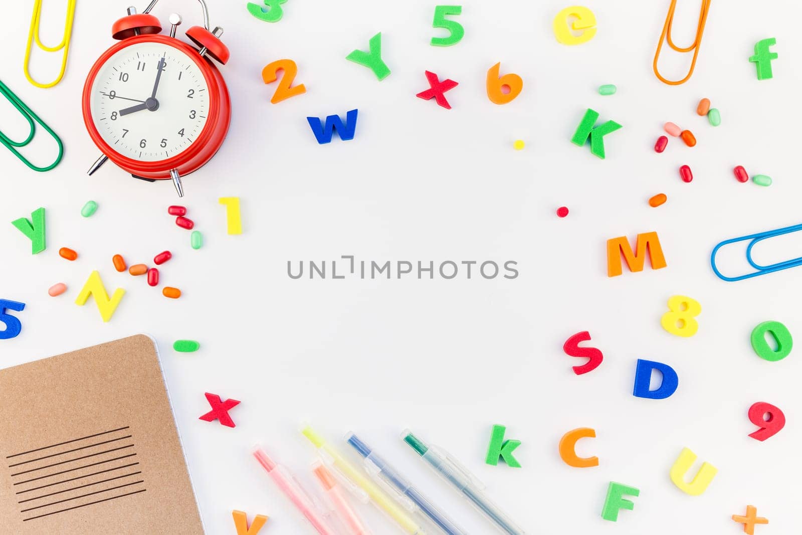 Creative flat lay back to school concept with alarm clock, color school and office supplies on white table background with copy space, frame, template for text or design