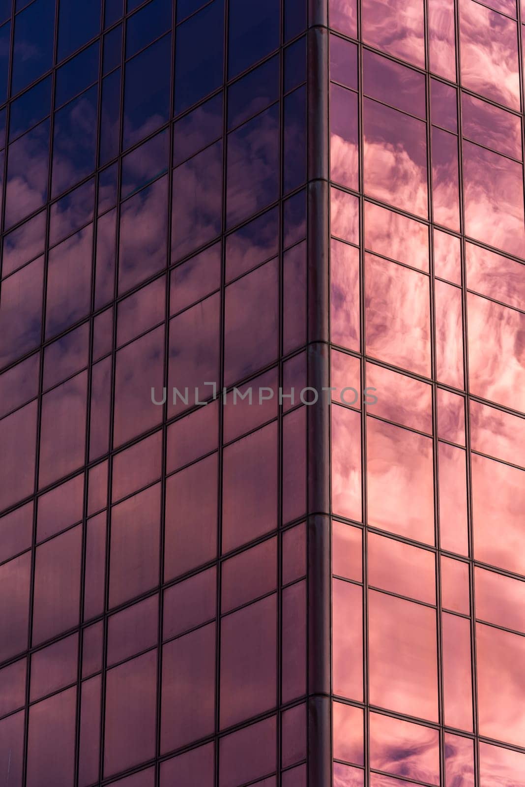 Sky and clouds reflected in windows of pink modern office building