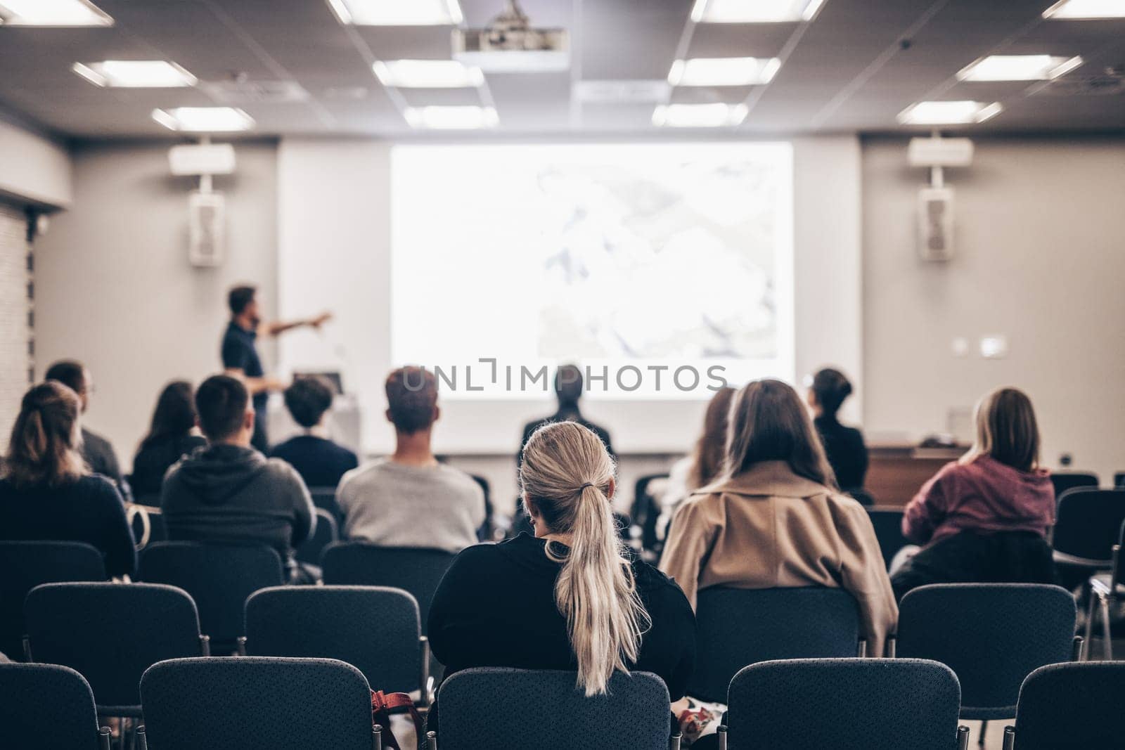 Speaker giving a talk in conference hall at business event. Rear view of unrecognizable people in audience at the conference hall. Business and entrepreneurship concept