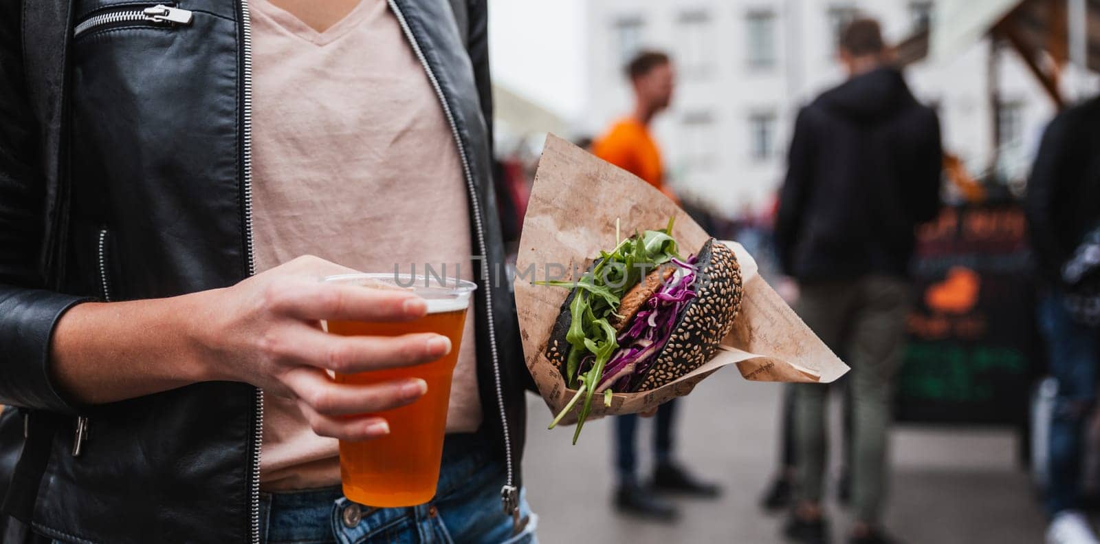 Close up of woman hands holding delicious organic salmon vegetarian burger and homebrewed IPA beer on open air beer an burger urban street food festival in Ljubljana, Slovenia