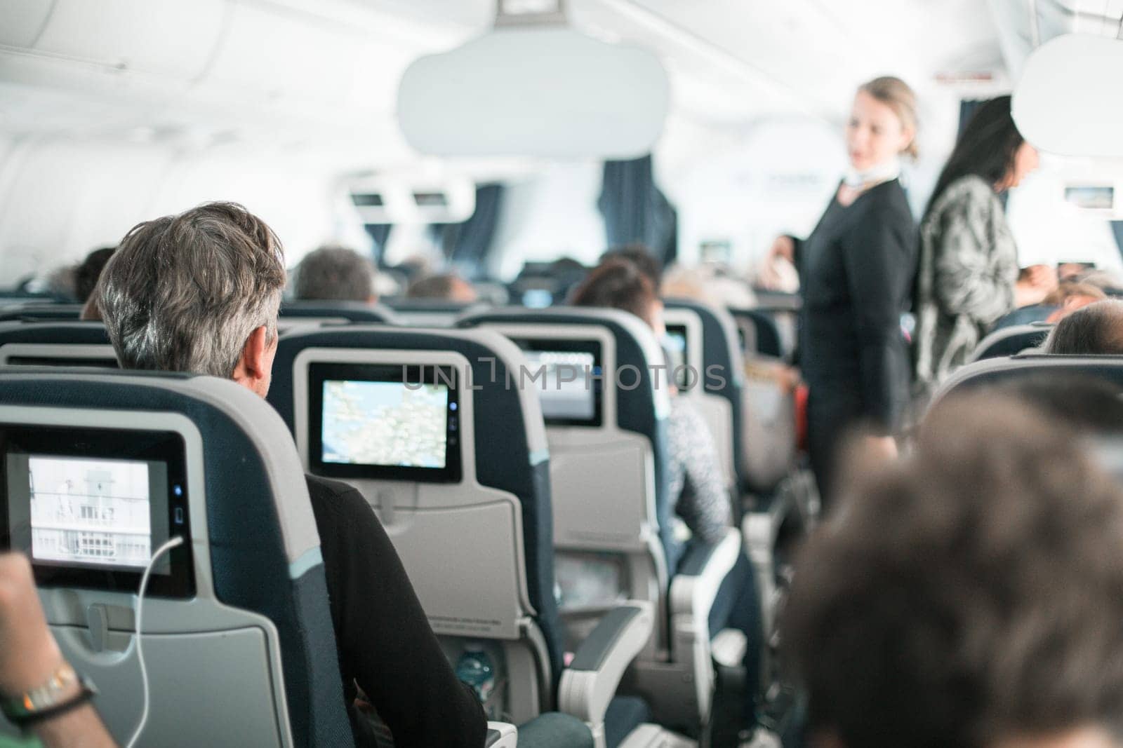 Interior of airplane with passengers on seats and stewardess in uniform walking the aisle, serving people. Commercial economy flight service concept
