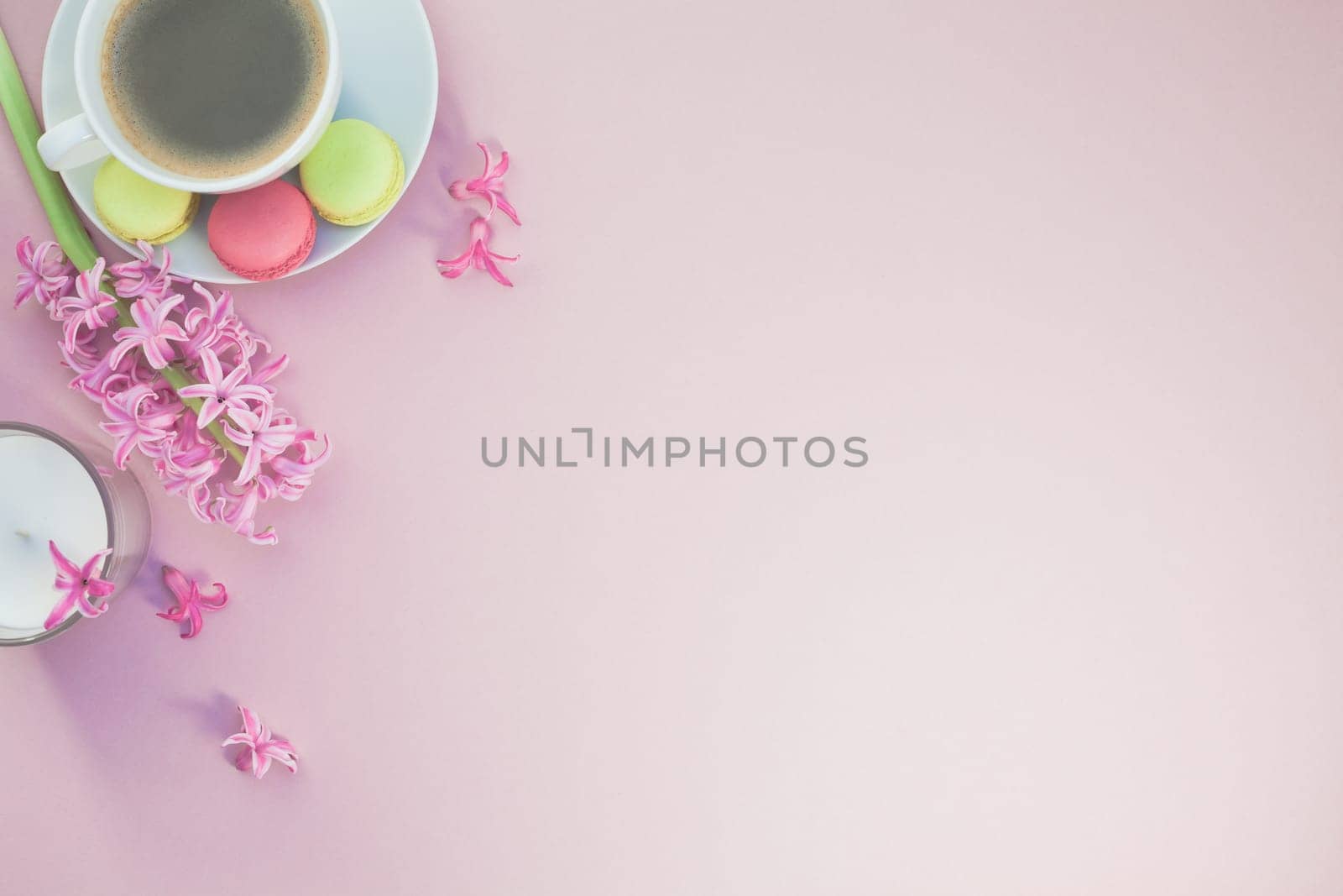 Creative flat lay photo of coffee cup with flowers, candle and macaroons with copy space on pink background minimal style