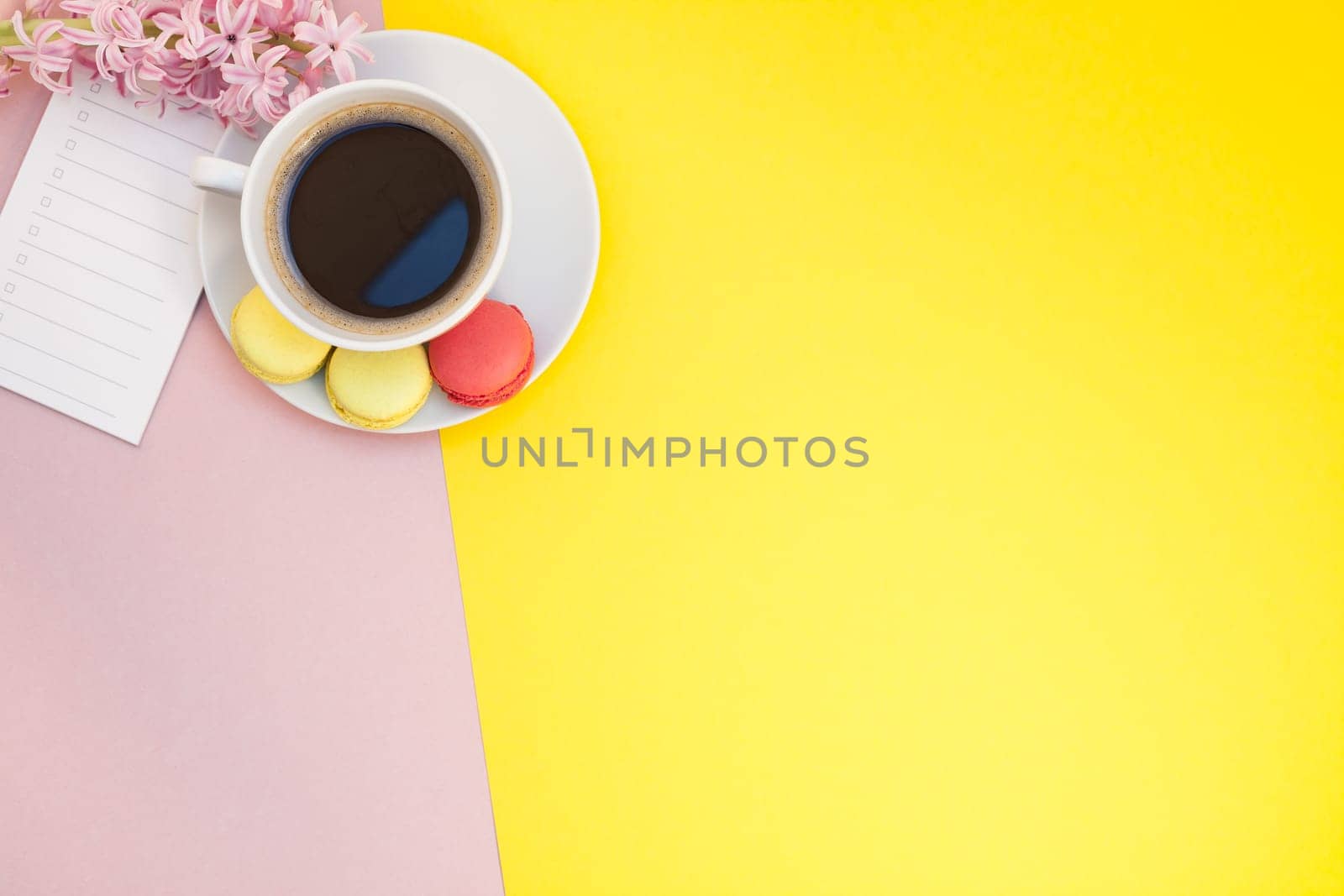 Creative flat lay photo of coffee cup with flowers, candle and macaroons with copy space on pink background minimal style