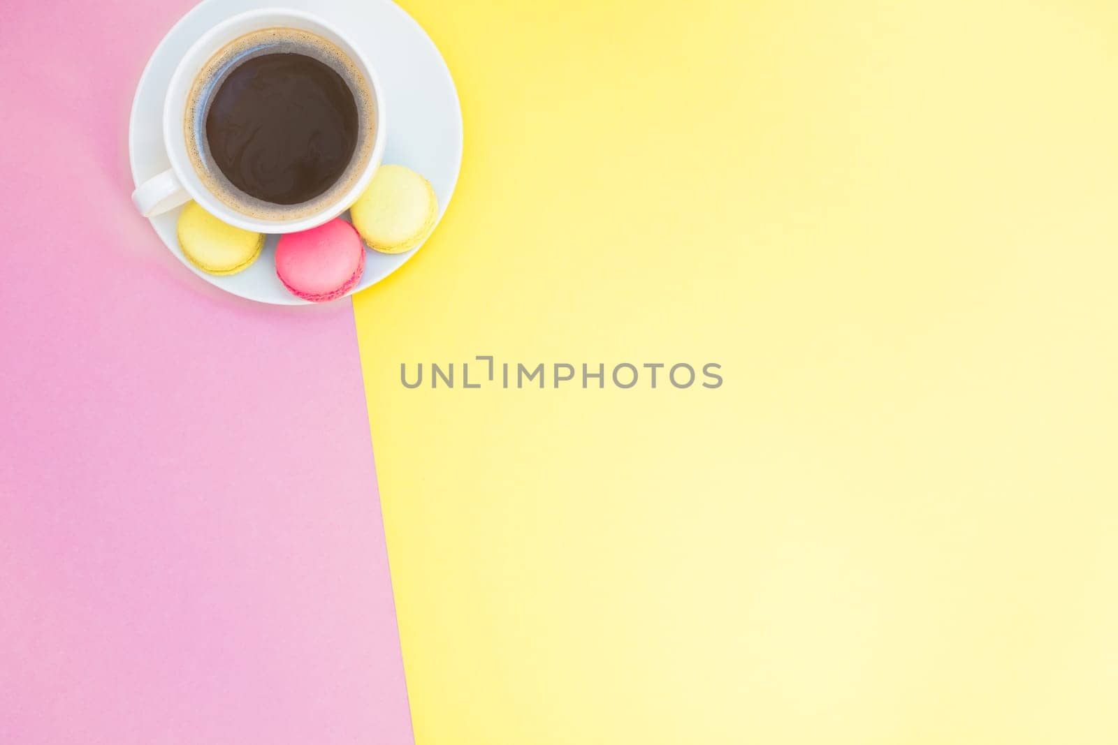 Creative flat lay photo of coffee cup and macaroons with copy space on pink and yellow background minimal style