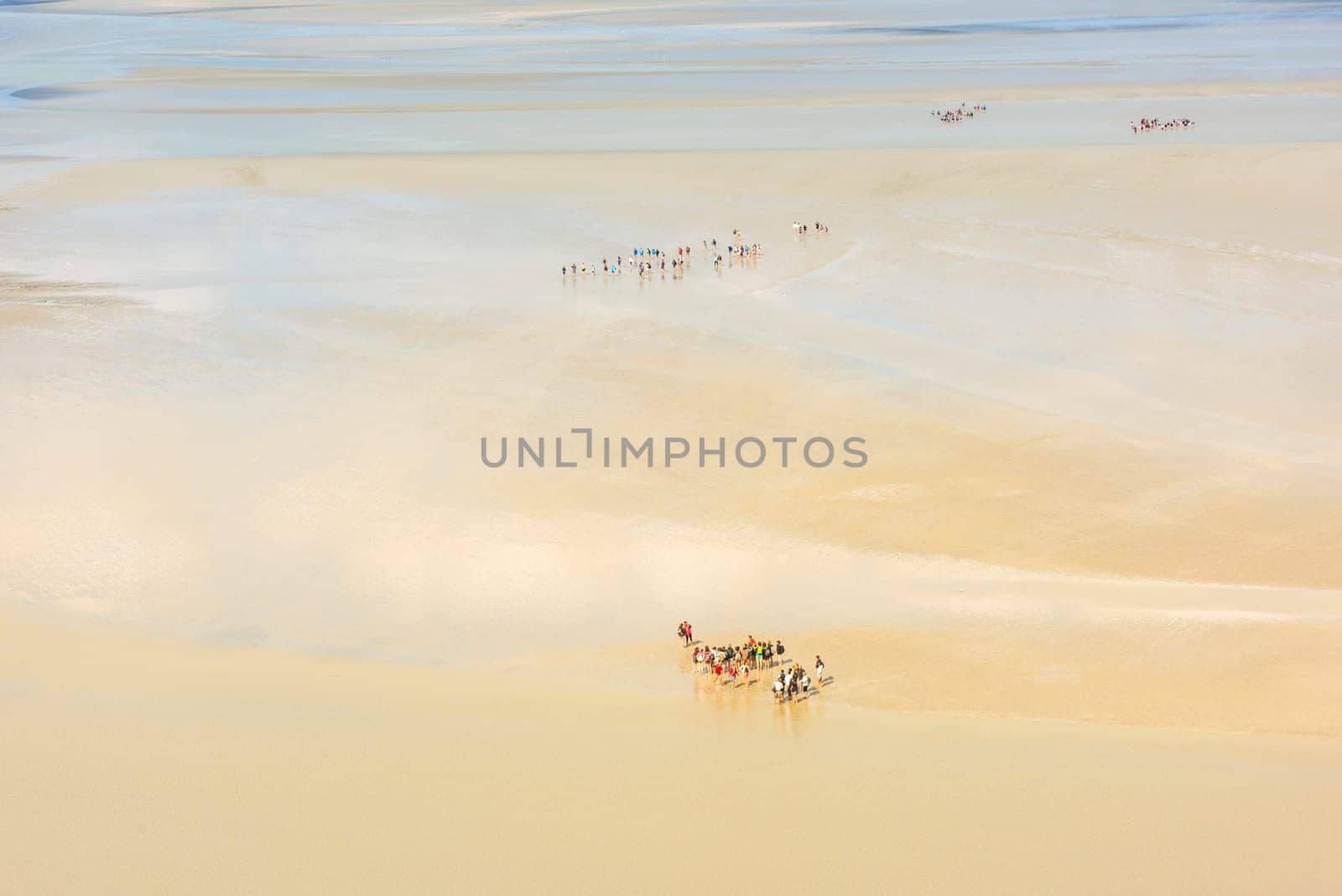 View from walls of Mont Saint Michel on the bay during the low tide with groups of tourists walking. France