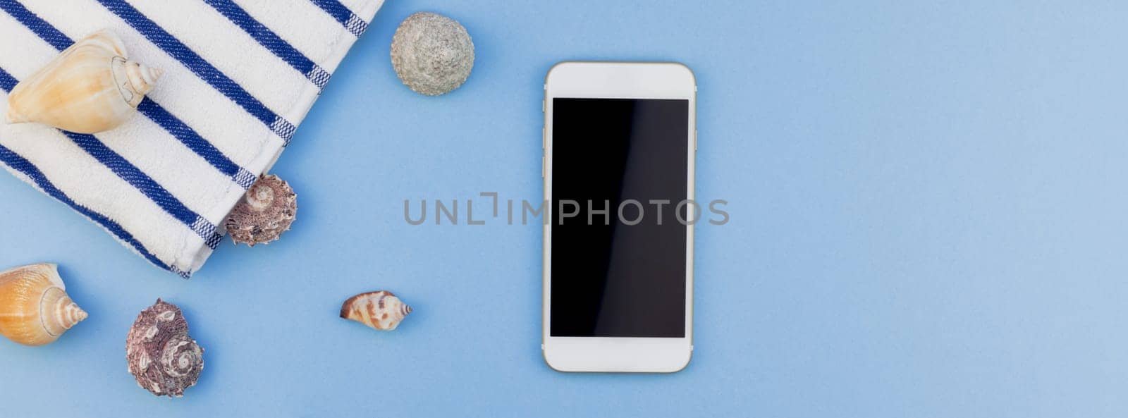 Creative long wide banner flat lay concept of summer travel vacations. Top view of beach towel, seashells, starfish and smartphone on pastel blue background with copy space in minimal style, template