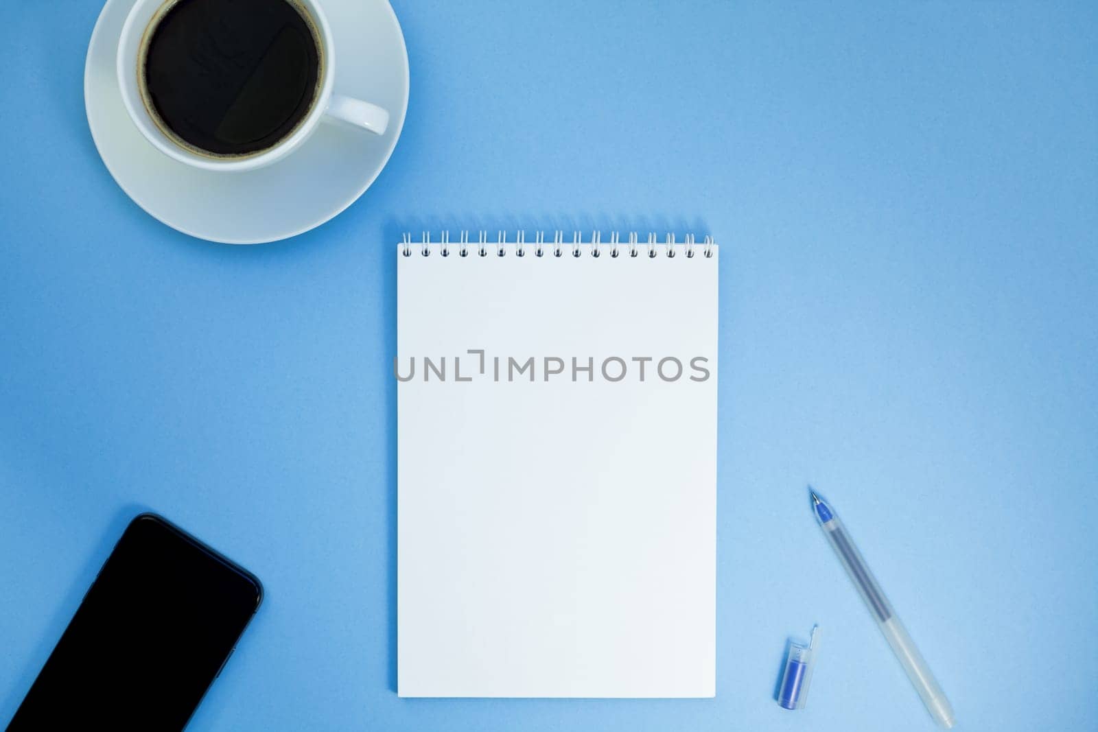 Creative flat lay photo of workspace desk with paper notebook, smartphone, earpieces, pen and coffee with copy space background minimal style