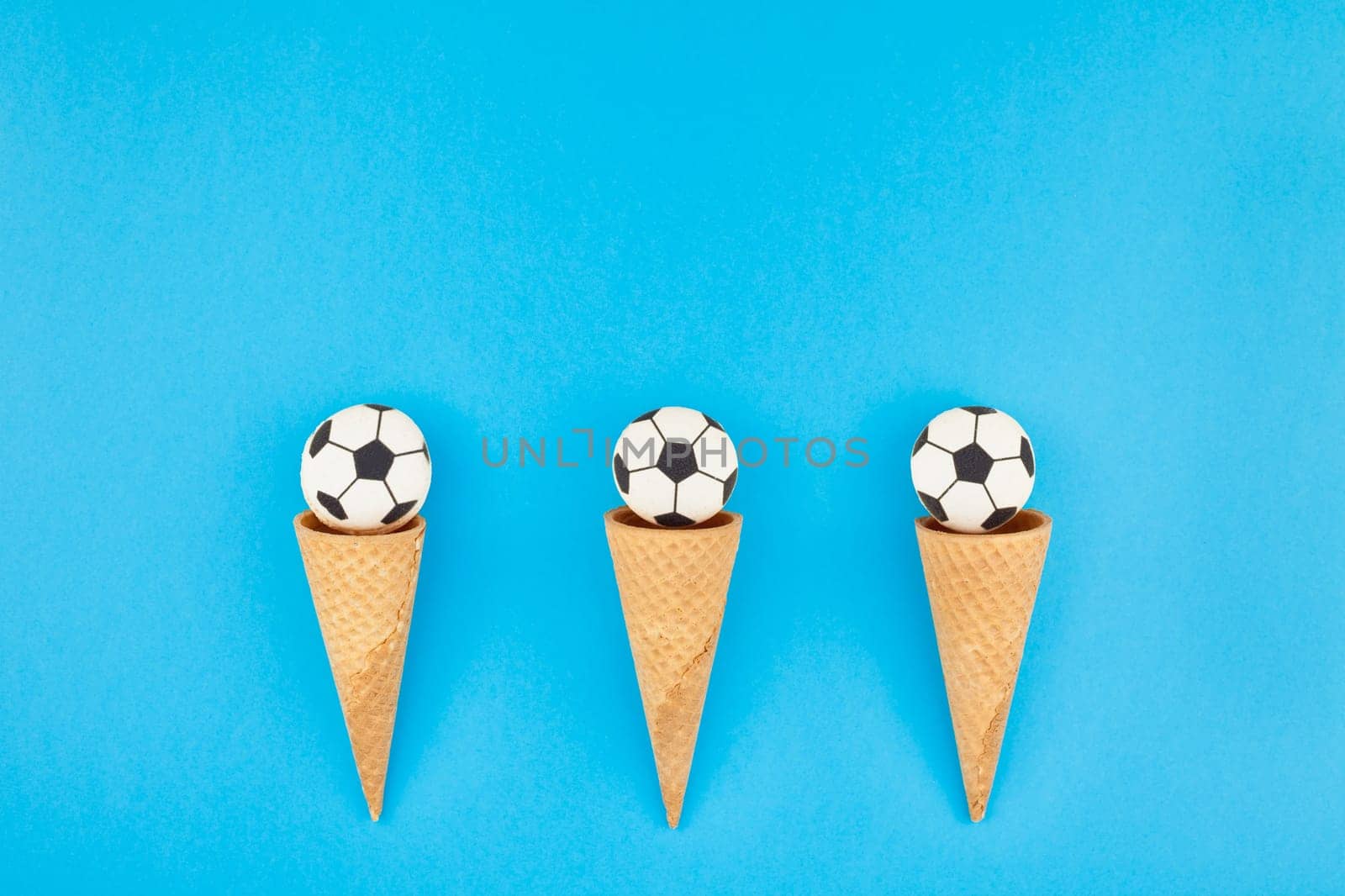 Creative flat lay top view of ice cream waffle cones with soccer balls macarons on bright bold blue background with copy space in minimal style, concept of football games for children birthday