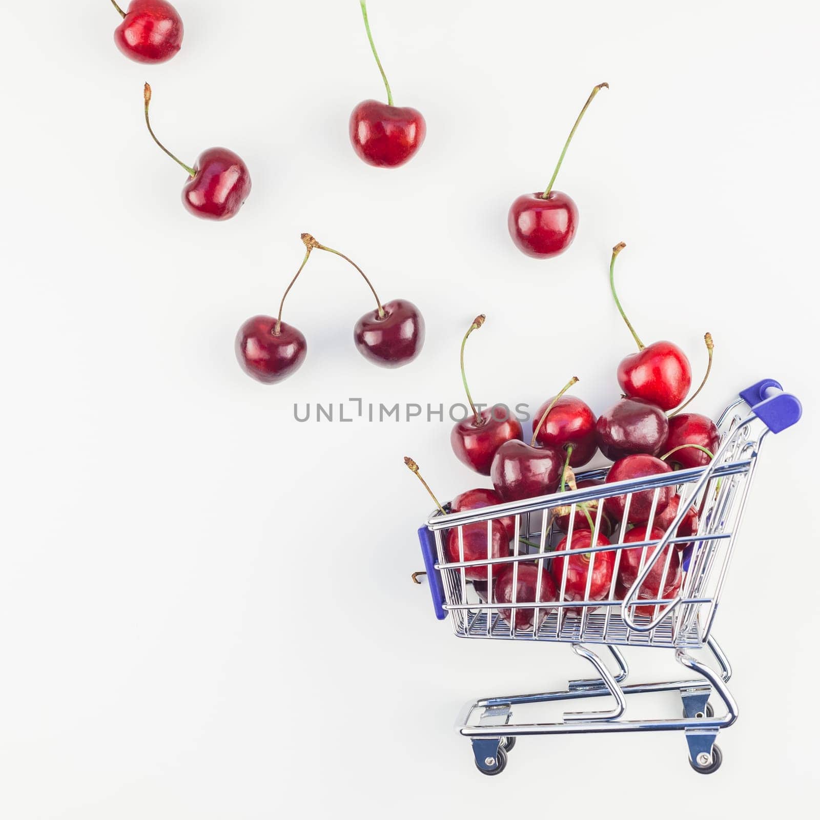Square image of ripe cherries in a shopping cart with copy space isolated on white background in minimal style. Concept of supermarket or fruit market shopping. Template for your text or design.
