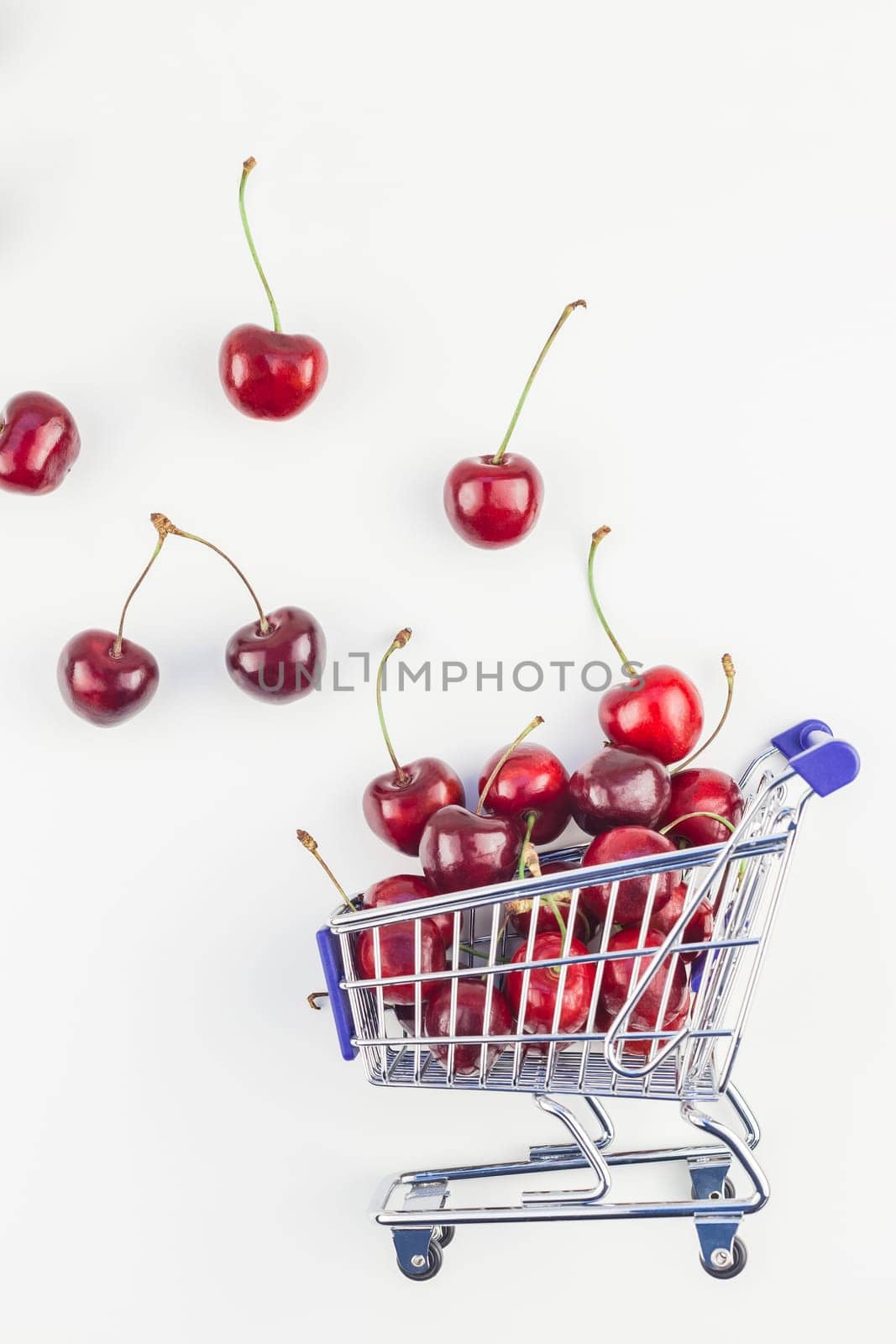 Creative image of ripe cherries in a shopping cart with copy space isolated on white background in minimal style. Concept of supermarket or fruit market shopping. Template for your text or design.