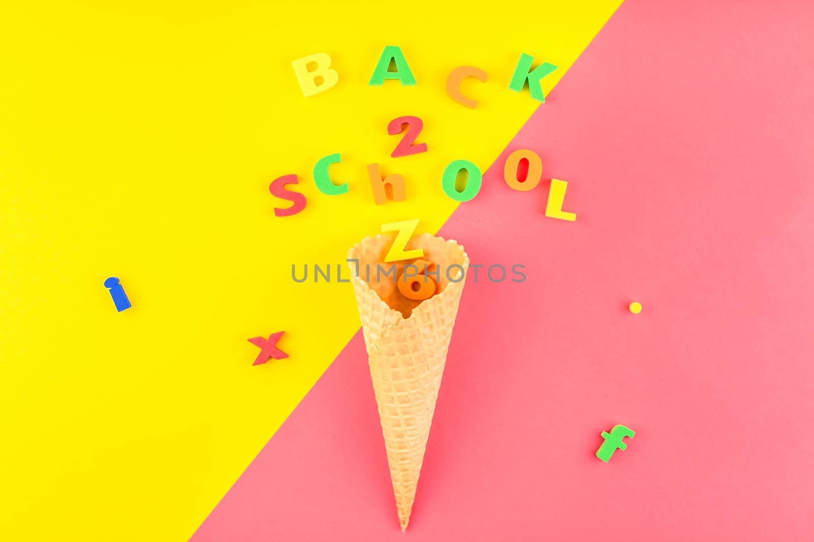 Creative flat lay back to school concept with waffle cone and welcome letters message on bright yellow and pink paper background with copy space, template for text or design