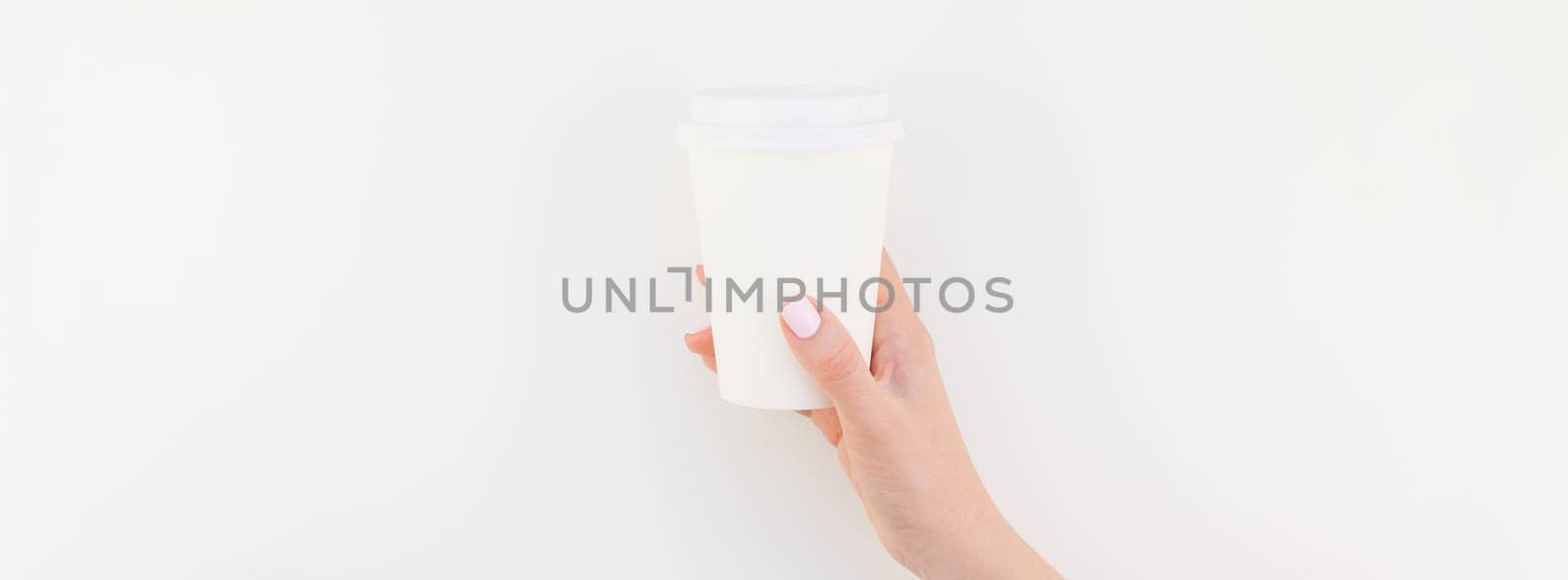 Long wide banner mock up of woman hand holding paper coffee cup with copy space isolated on white background in minimalism style. Template for feminine blog, social media