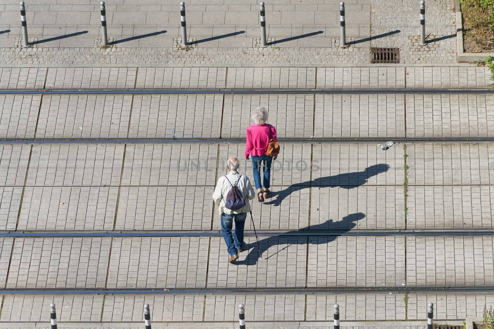 Old pensioner couple crossing the tracks of a streetcar on their way through the city center