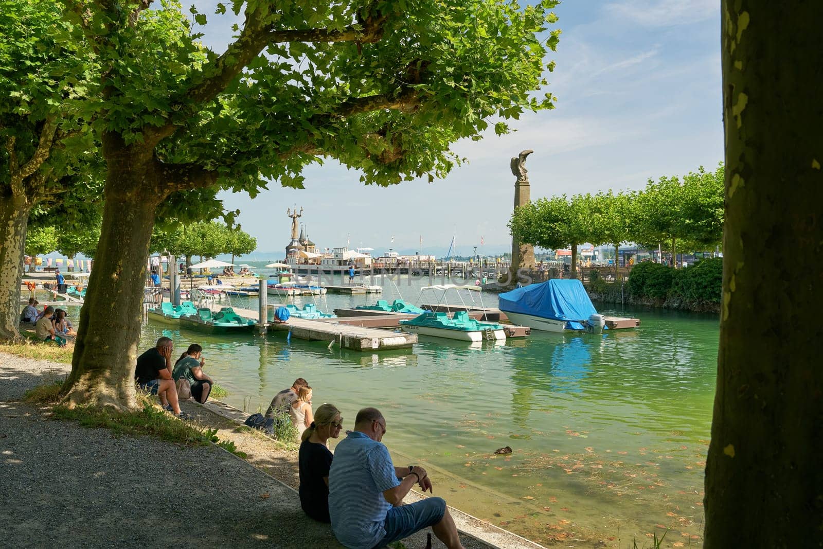Tourists relax under trees on the shores of Lake Constance at the port of Constance