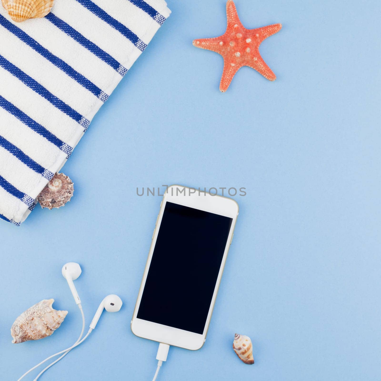 Creative square flat lay concept of summer travel vacations. Top view of beach towel, seashells, starfish and smartphone on pastel blue background with copy space in minimal style, template for text