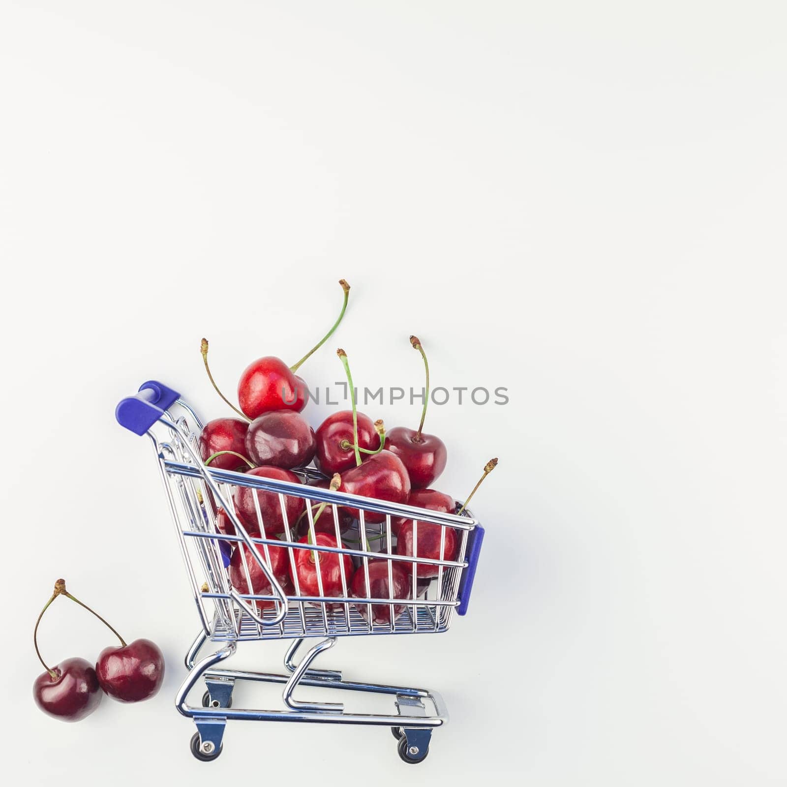 Square image of ripe cherries in a shopping cart with copy space isolated on white background in minimal style. Concept of supermarket or fruit market shopping. Template for your text or design.
