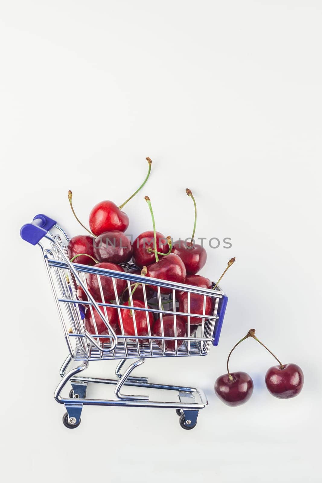 Creative image of ripe cherries in a shopping cart with copy space isolated on white background in minimal style. Concept of supermarket or fruit market shopping. Template for your text or design.