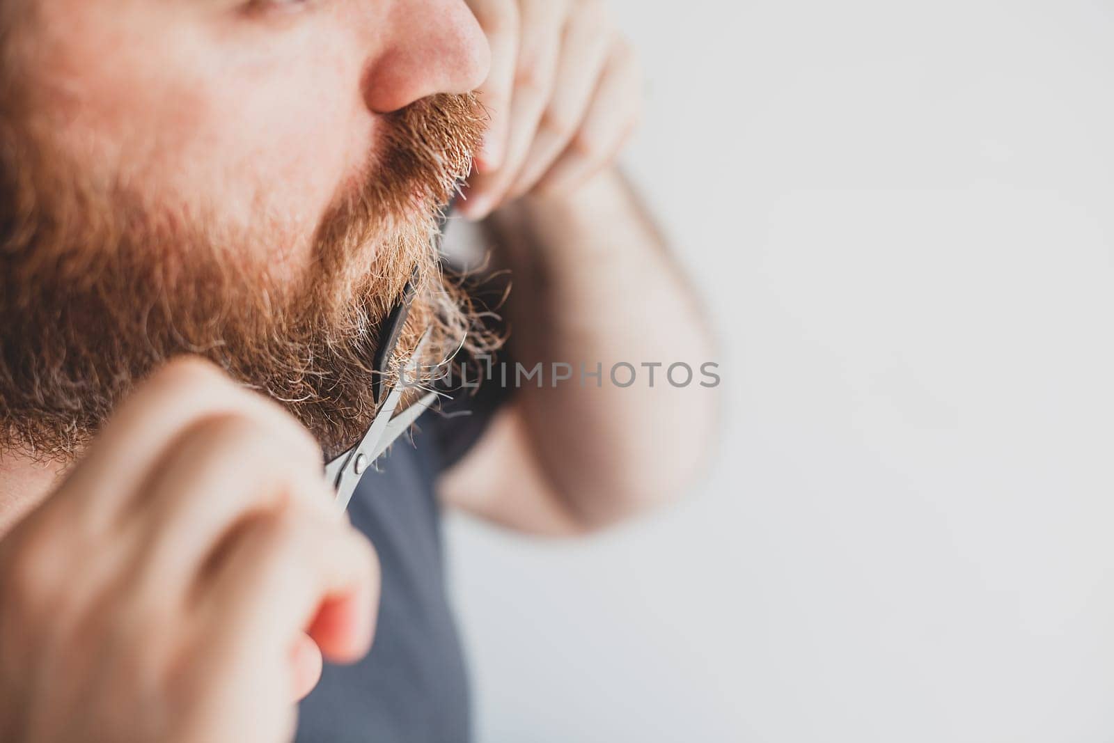 Selfcare during quarantine isolation. Adult handsome caucasian man cutting moustache and beard himself personally with scissors at home. Coronavirus outbreak and people shutdown, stay home concept