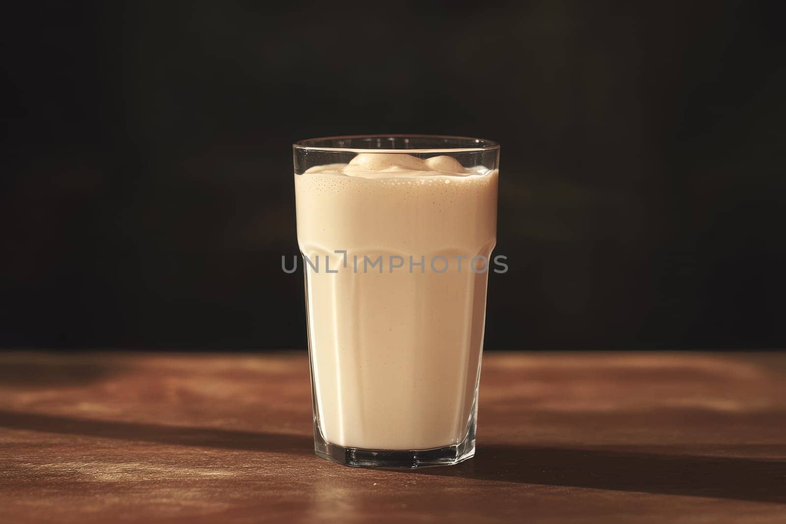 This minimalist glass showcases a delicious, creamy milkshake, resting on a wooden table in a warm and inviting atmosphere, perfect for enjoying a sweet treat.