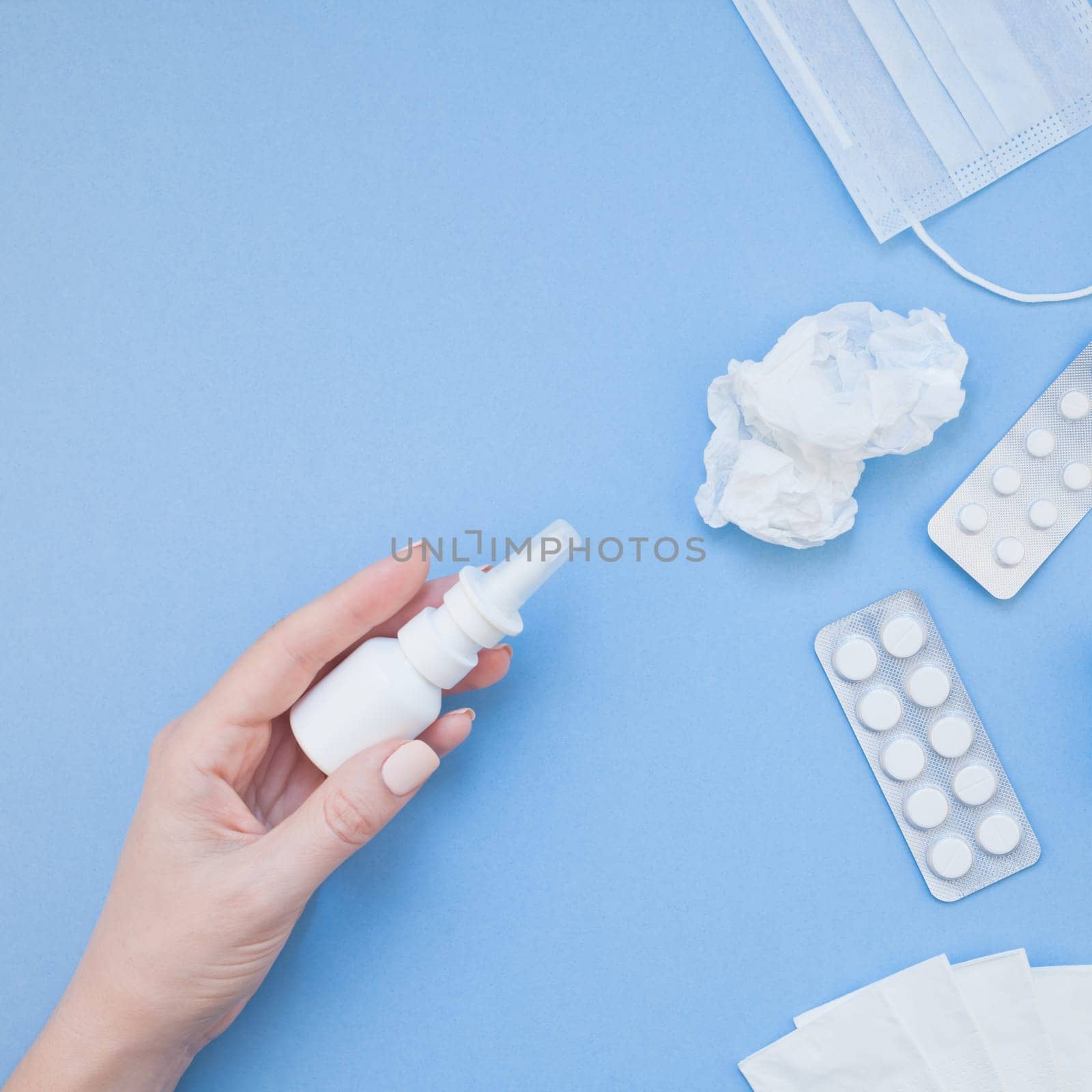 Creative flat lay concept of seasonal spring allergy with napkins, pills, face mask, drops in a bottle and a female hand with square copy space background minimal style, template for text