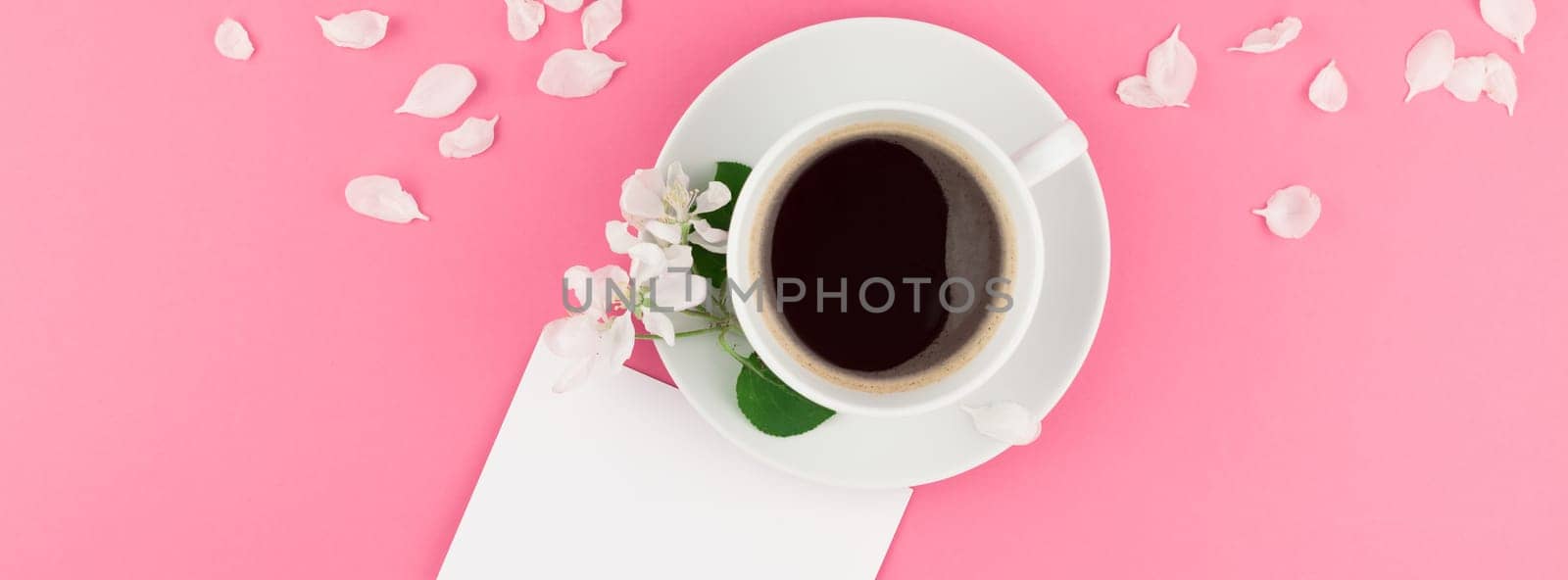 Creative flat lay concept top view of coffee cup and white apple tree flowers petals on pastel pink background with postcard mock up and copy space in minimal style template for text. Long wide banner