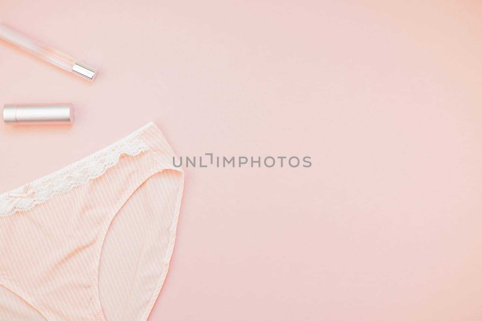 Feminine flat lay set of female panties and accessories, perfumes, lipstick on pastel pink color background for fashion blog and social media with copy space for text