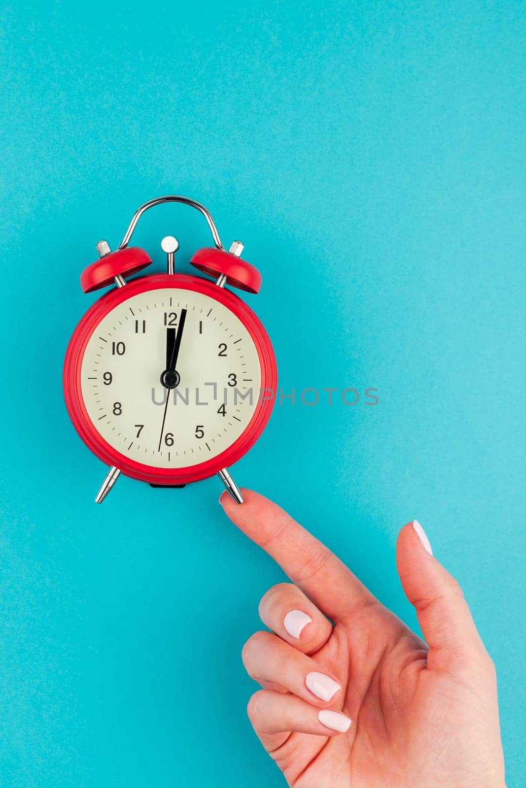 Creative flat lay concept top view of woman hand holding the red vintage alarm clock on bright blue turquoise color paper background with copy space in minimal style, template for text