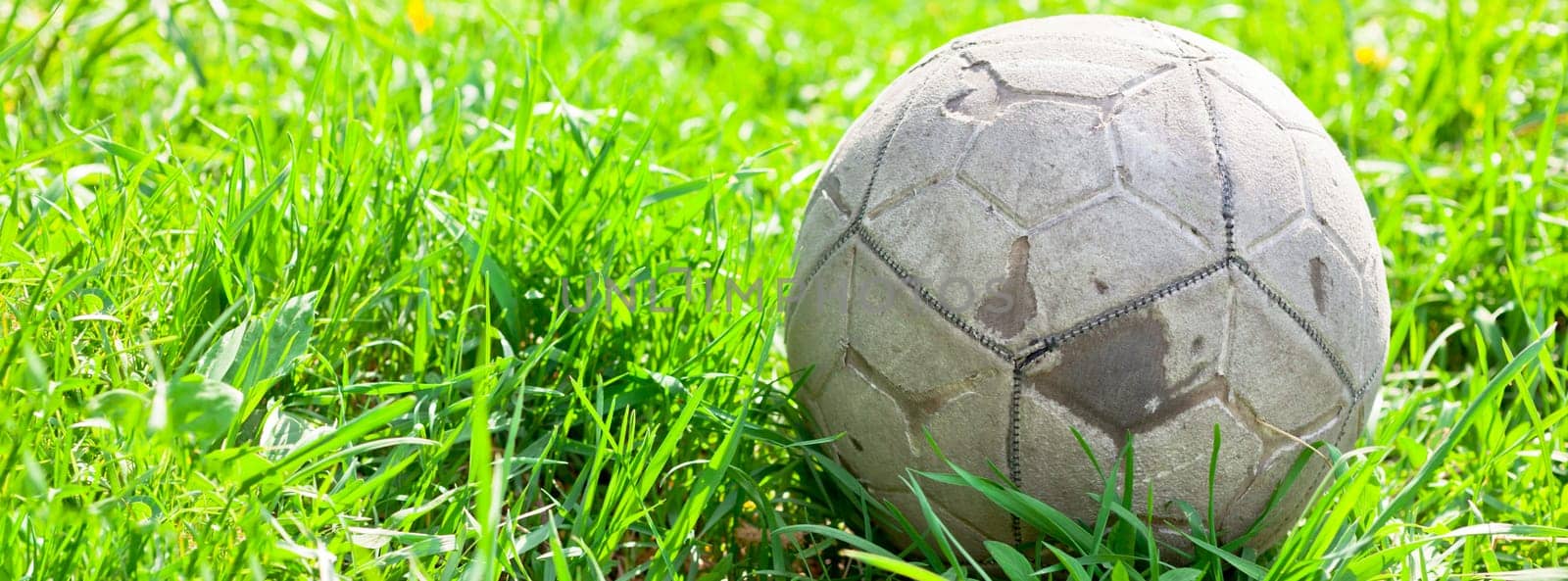 Old soccer ball forgotten in the green grass field. The football concept. Long wide banner