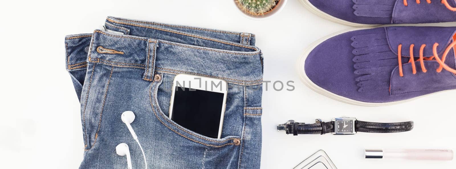 Long wide banner Flat lay of suede shoes, blue jeans, bracelets cactus and smartphone headphones on white background with copy space. Overhead view of woman casual outfit. Trendy hipster look top view