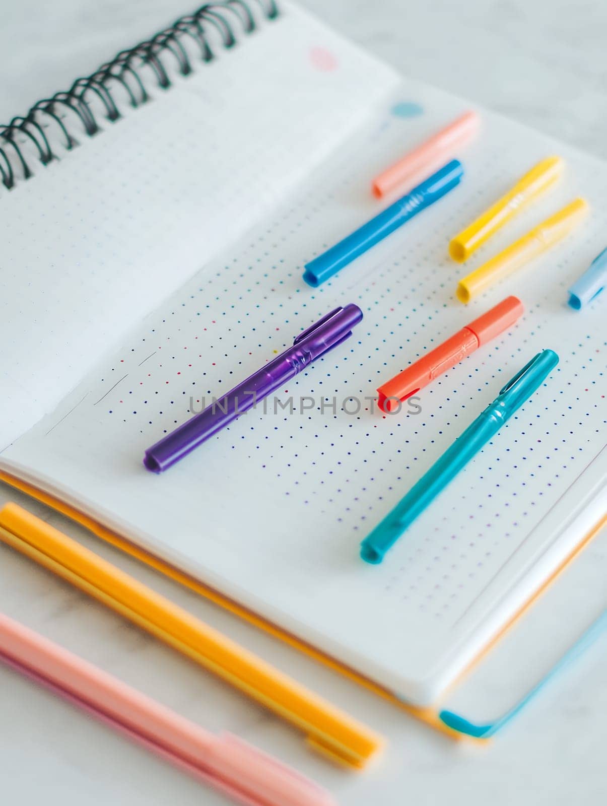 A dotted notebook with vibrant pens on a white surface, perfect for bullet journaling and creative projects.