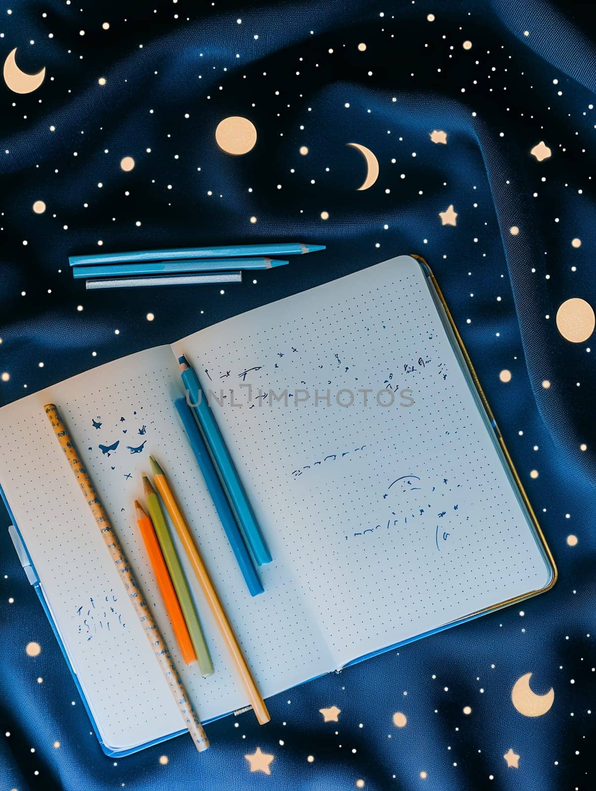Open journal with pencils on a starry night-themed fabric, evoking creativity and imagination.