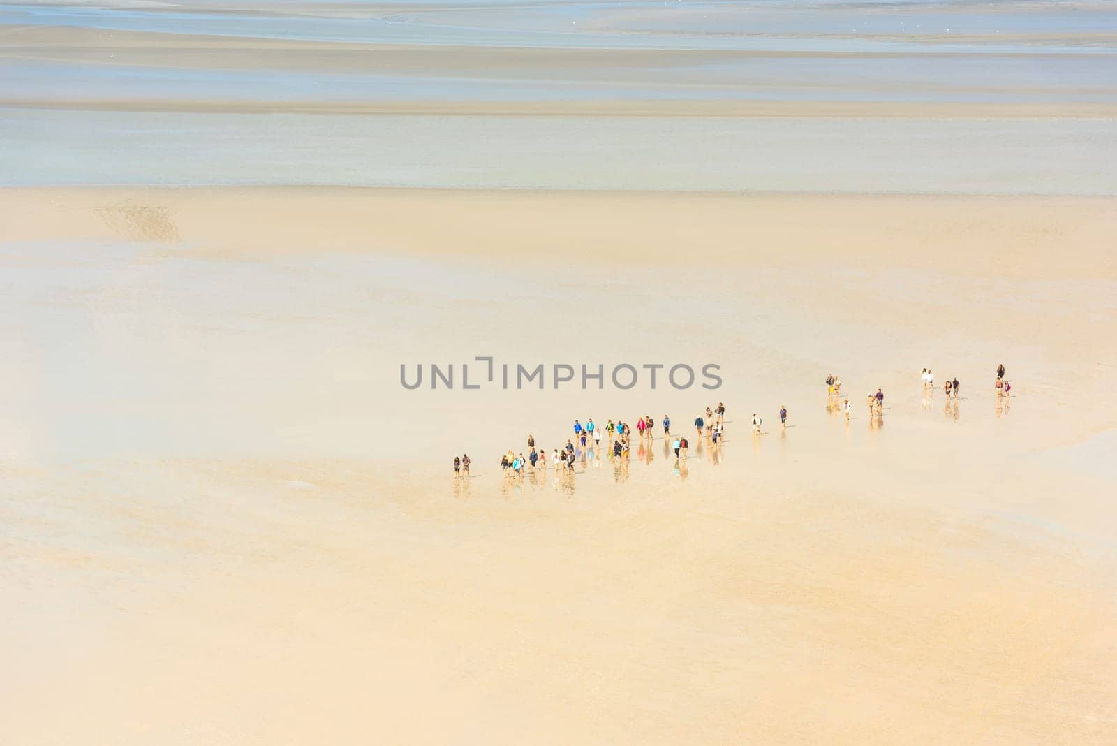 View from walls of Mont Saint Michel on the bay during the low tide with groups of tourists walking. France