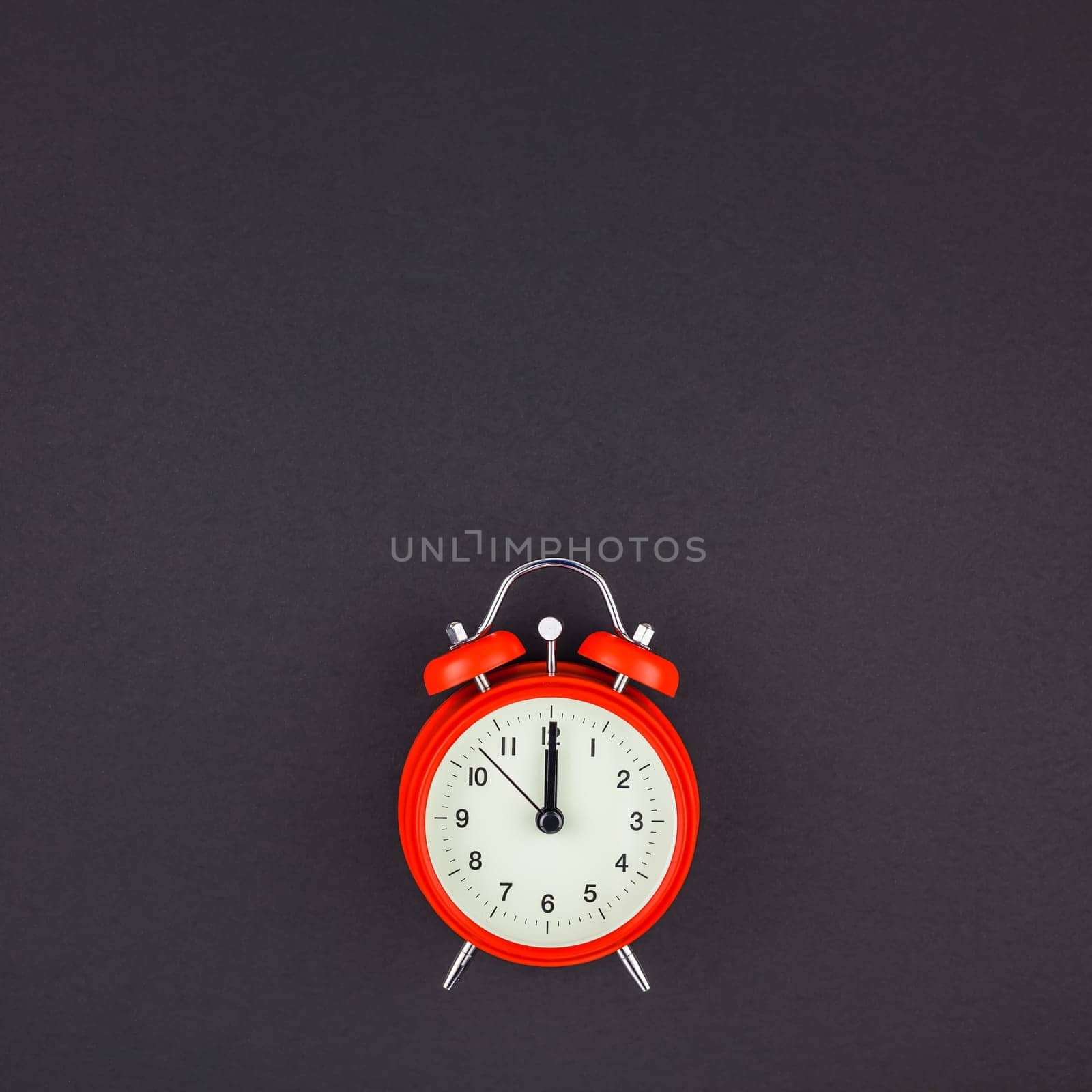 Concept image of a red vintage alarm clock with twelve o clock on dark black color paper background with copy space in minimal style, square template for text