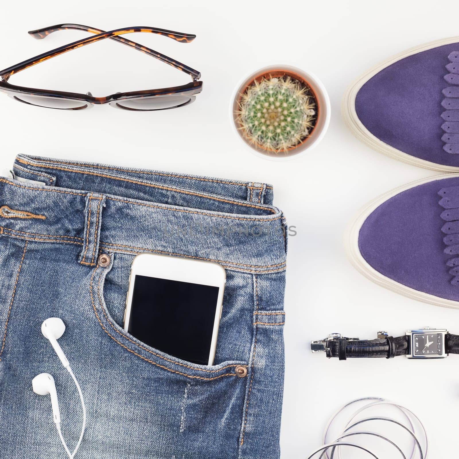 Square Flat lay of suede shoes, blue jeans, bracelets cactus and smartphone with headphones on white background with copy space. Overhead view of woman casual outfit. Trendy hipster look top view