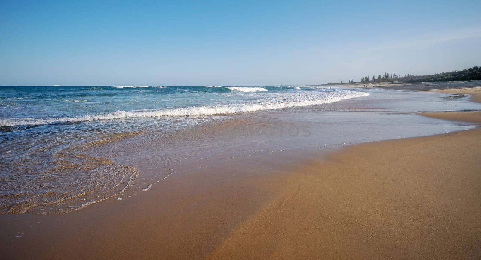 Popular tourist area, sandy beach with surf waves rolling in at Buddina, Sunshine Coast, Queensland, with clear, blue sky