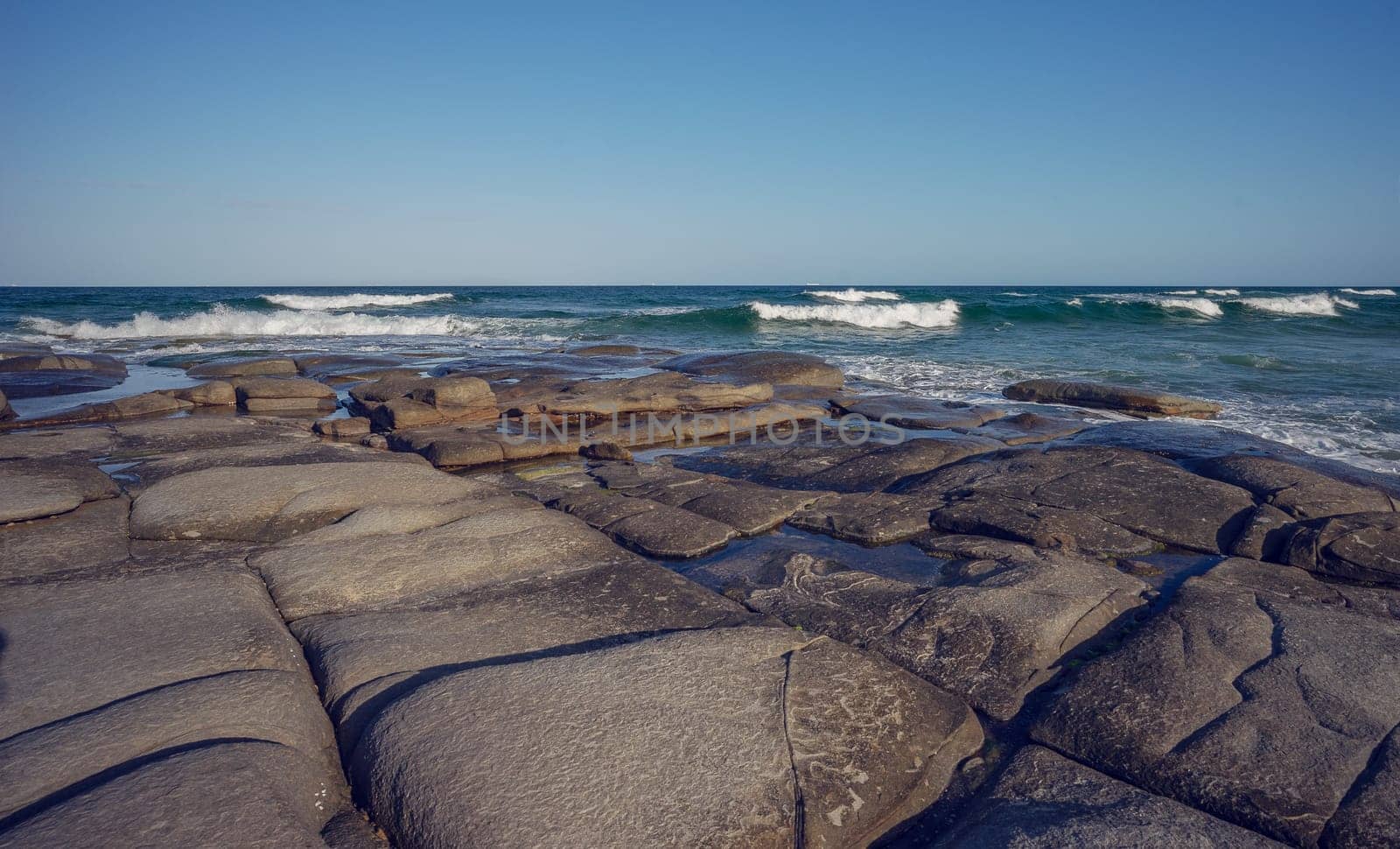 The rocky headland at Point Cartwright juts out into the sea with surf waves crashing over it. The smooth surface of the rocks make easy walking to explore it's rockpools.