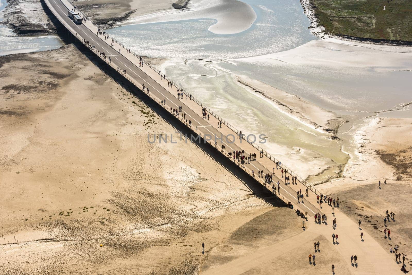 View from walls of Mont Saint Michel on the bay during the low tide. Groups of tourists walking. France