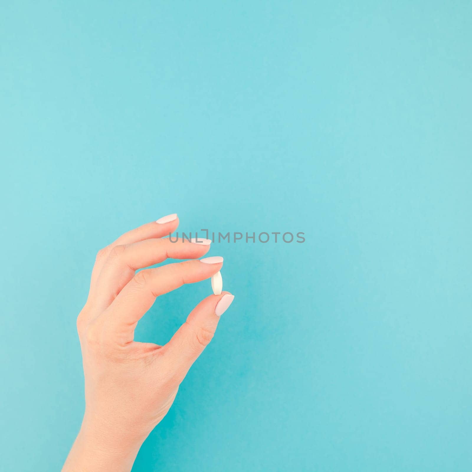 Woman hand holding a white pill on pastel blue paper background with copy space in minimal style, square template for text. Concept of medical treatment, pharmacy, healthcare