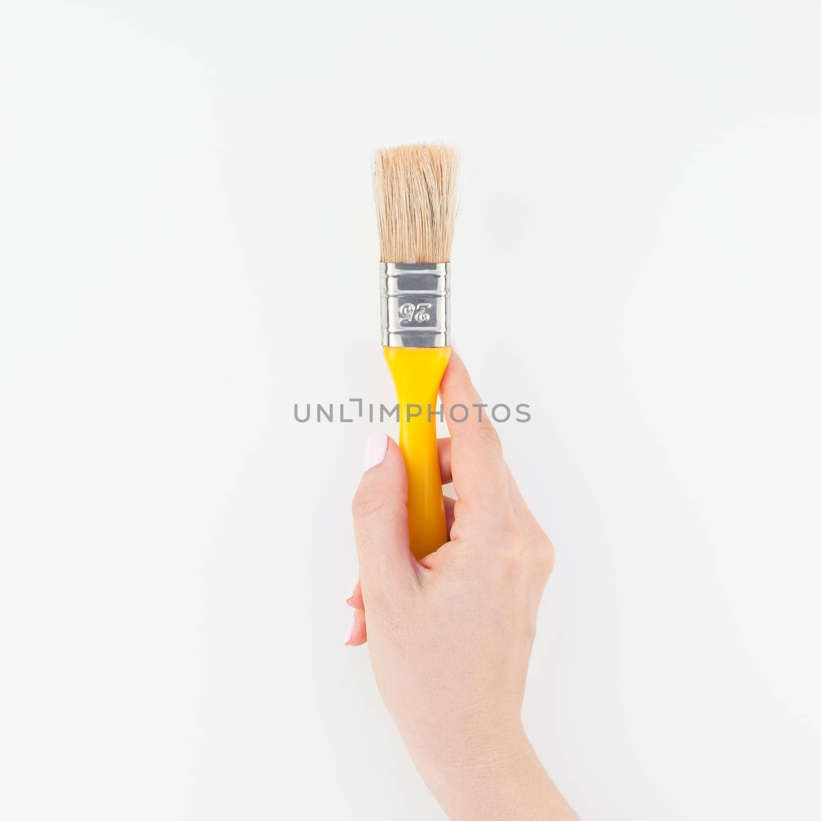 Square image of woman hand holding new paint brush with copy space isolated on white background in minimalism style. Template for feminine blog, social media. Repair or improvement concept