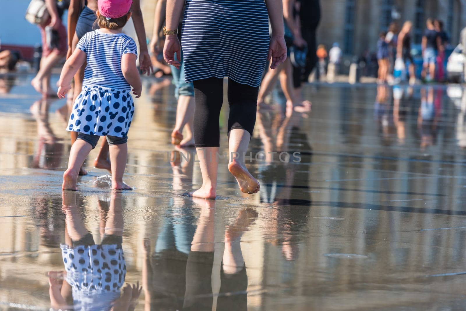 People having fun in a mirror fountain in front of Place de la Bourse in Bordeaux, France