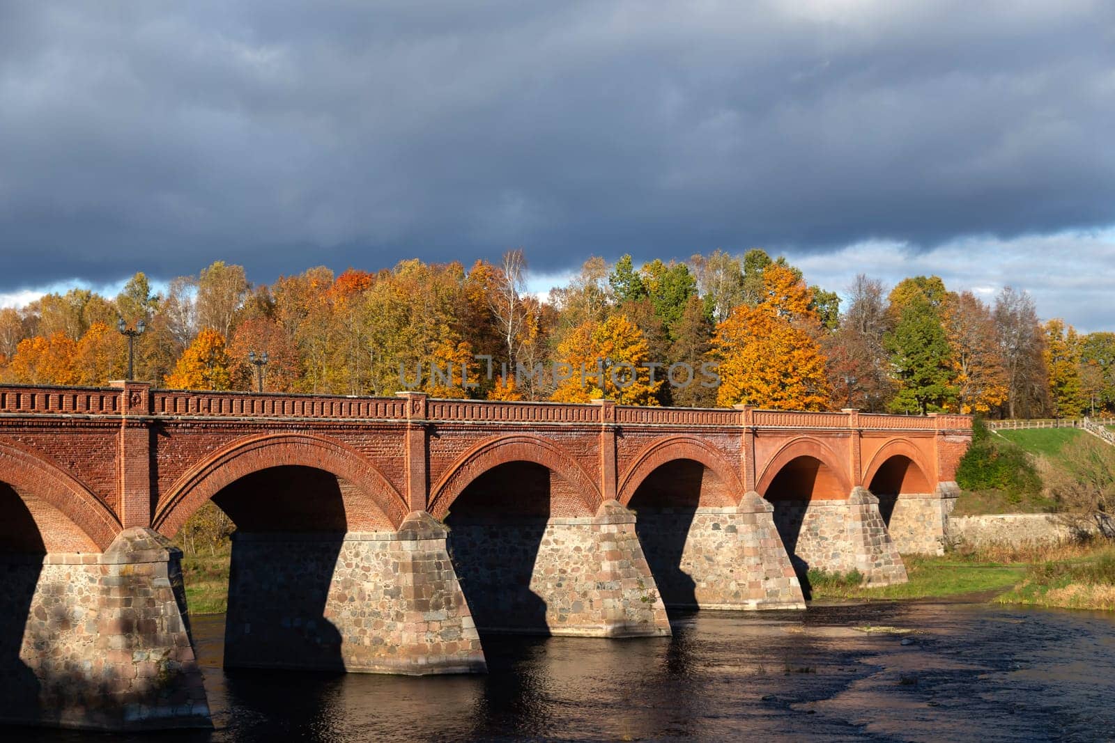 Autumn October landscape with yellowed foliage against the backdrop of an old brick bridge across the river