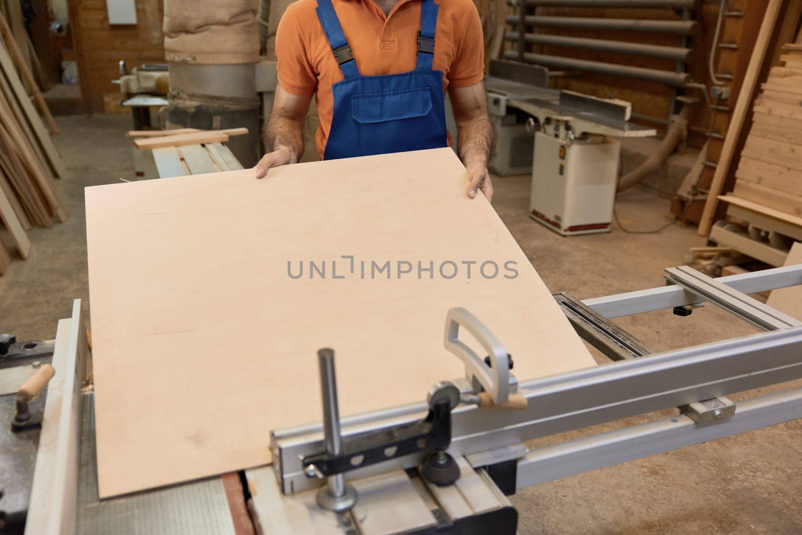 Crop shot of craftsman in uniform and protective goggles cutting woods on pieces working at circular cutting table in furniture factory workshop