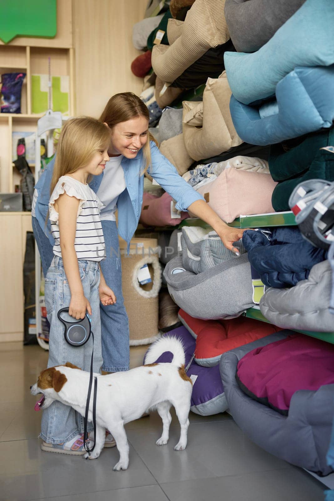 Happy family doing shopping at pet store. Happy interested mother and little daughter choosing bedding for lovely dog on shelves