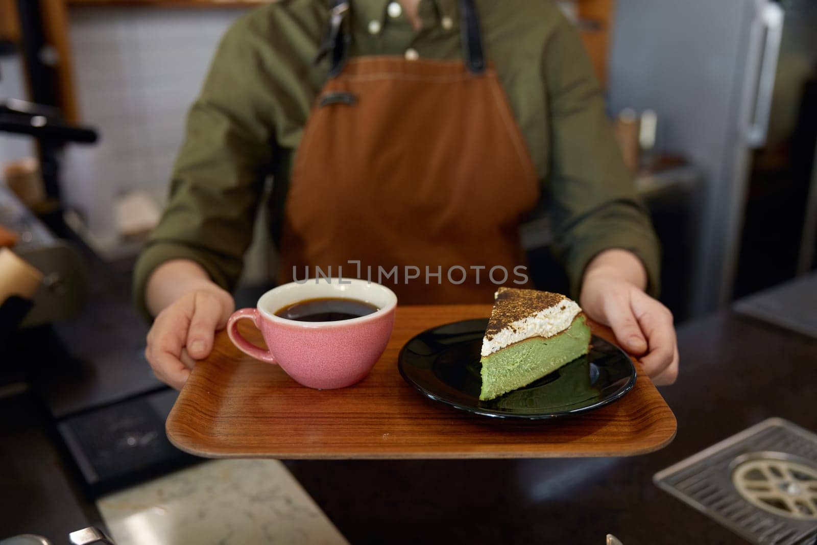 Cropped shot of woman barista giving wooden tray with freshly brewed coffee drink in ceramic cup and cake piece portion on plate. Client service at cafeteria or restaurant